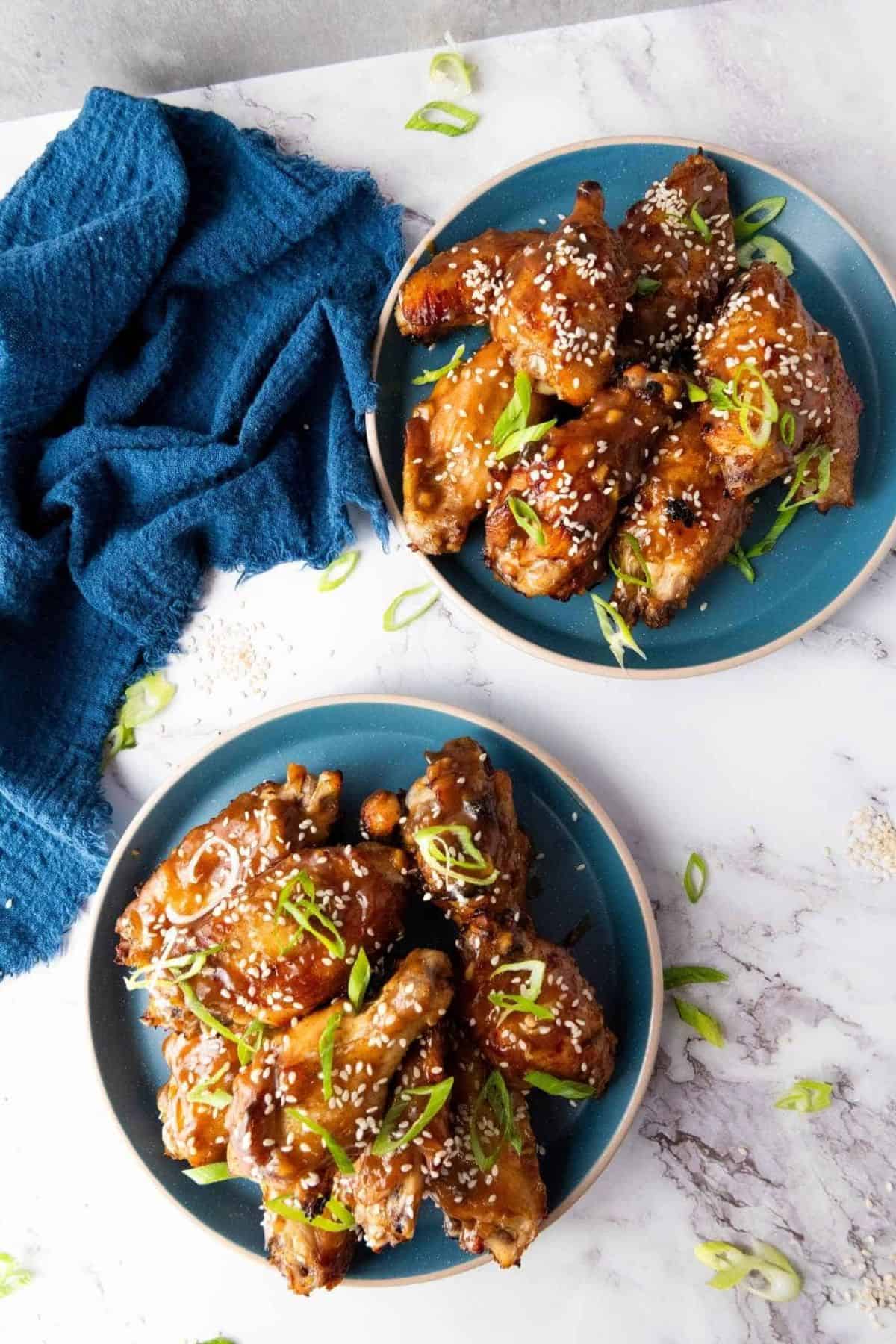 Two plates of stacked Baked Asian Sticky Chicken Wings with a table napkin on the side.