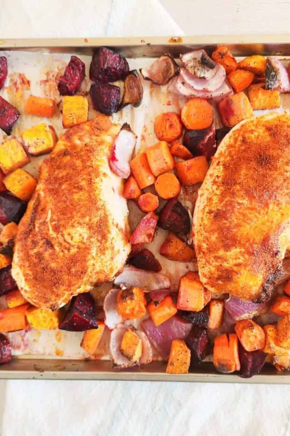 One Pan Roasted Chicken and Vegetables with golden chicken pieces and a mix of roasted zucchini, carrots, broccoli, and bell peppers on a baking sheet.