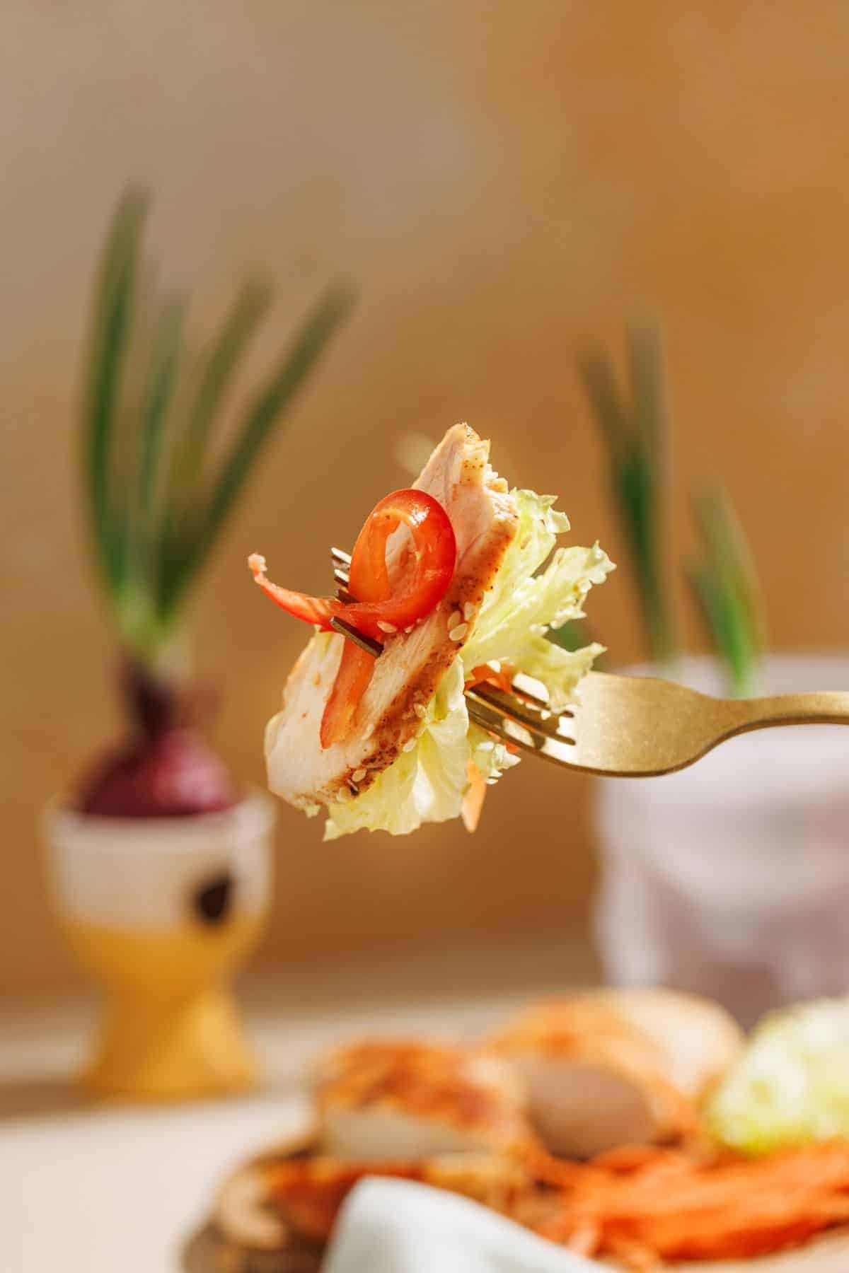 A fork lifting a portion of Asian Sesame Chicken Salad with chicken and crisp vegetables.
