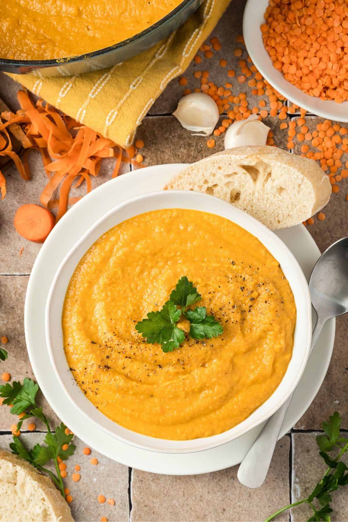 Cozy Carrot and Lentil Soup with a Sweet Apple Twist served in a bowl, surrounded with fresh carrots, lentils, and apple slices.