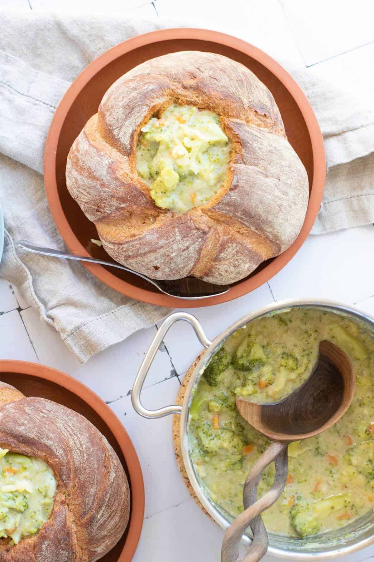 A sourdough bread bowl filled with creamy Broccoli Cheddar Soup and a pot filled with soup.