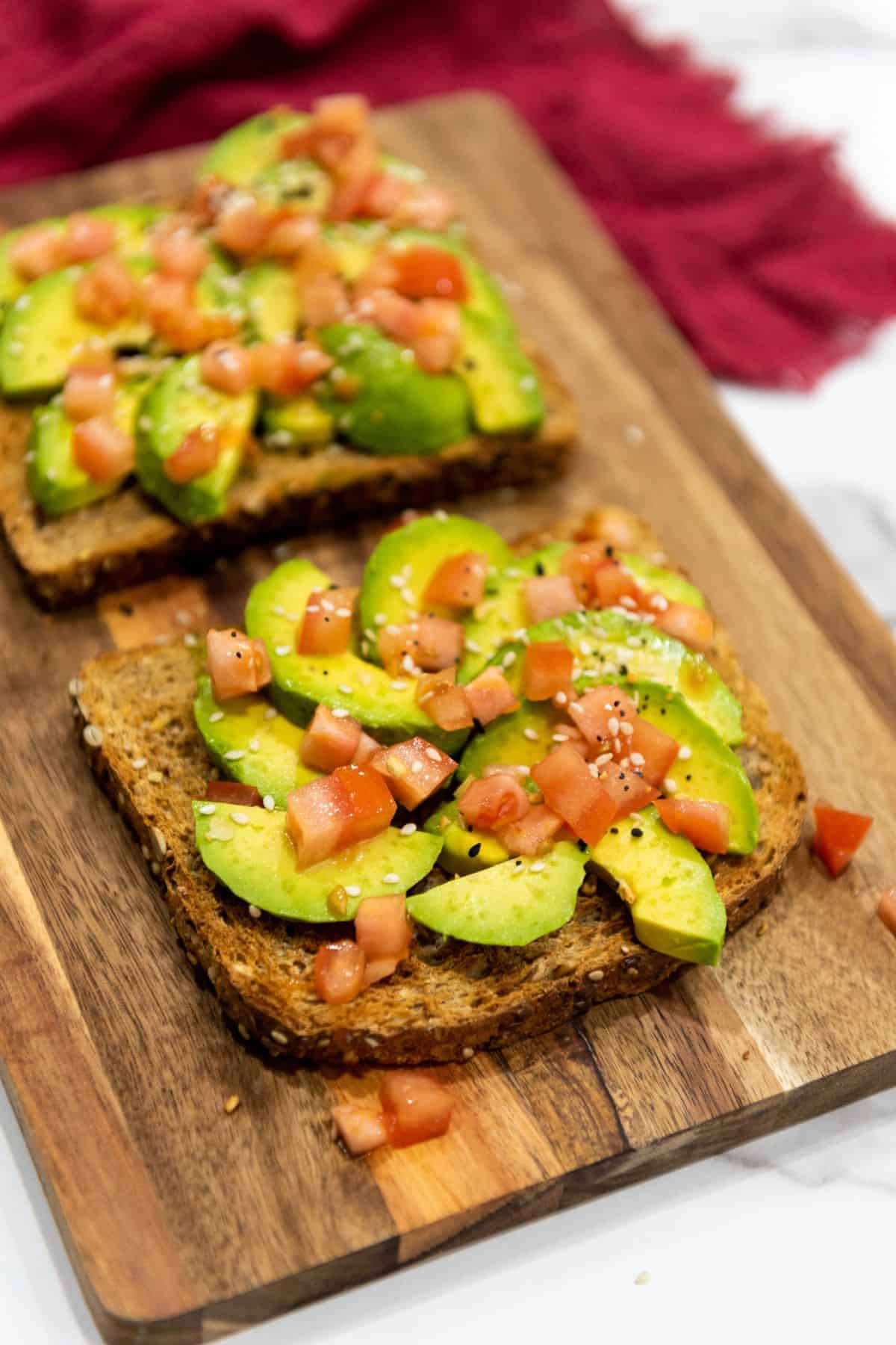 Toast on a wooden board topped with avocado slices and cherry tomato halves.