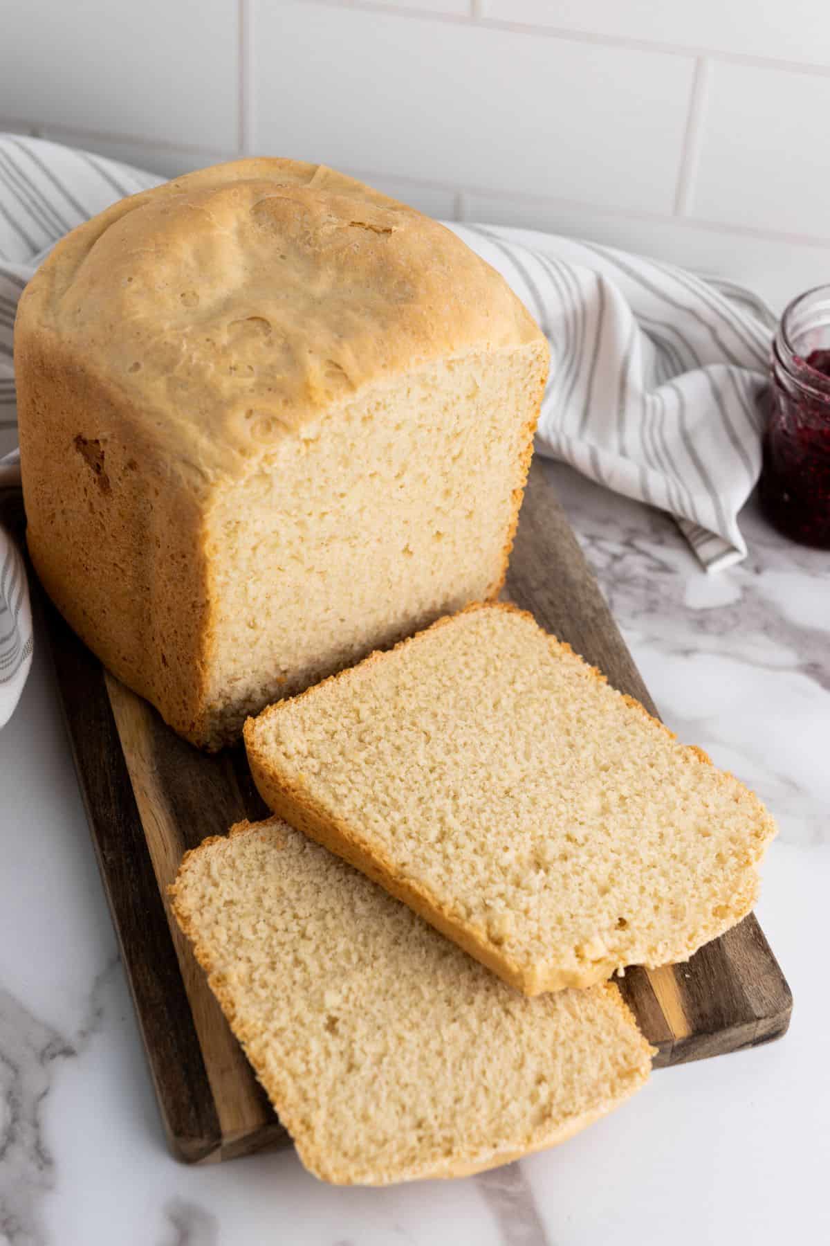 Loaf of bread being sliced on a wooden board with a cloth in the background.