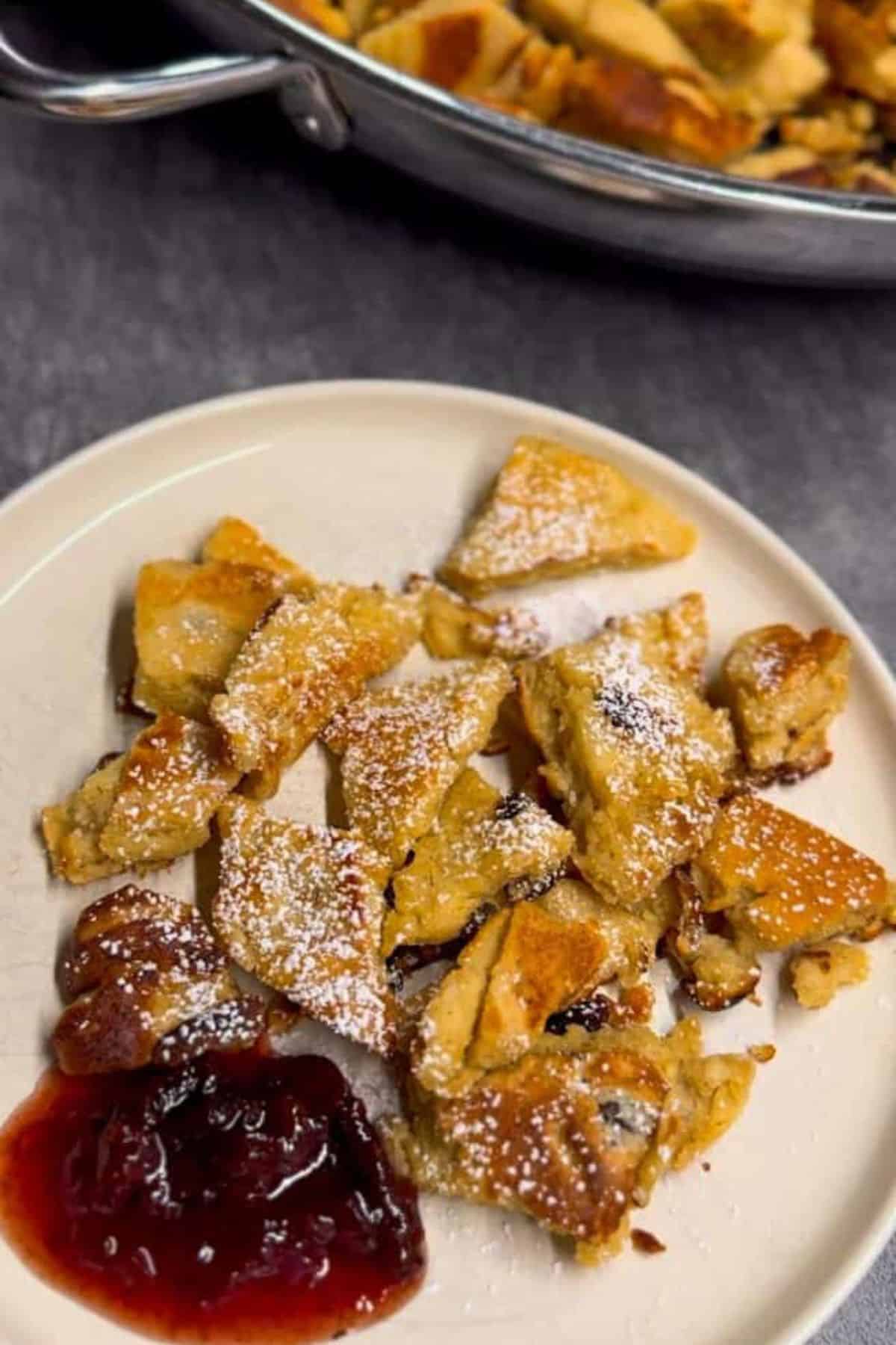 Fluffy shredded pancake on a plate, topped with powdered sugar and served with jam on the side.