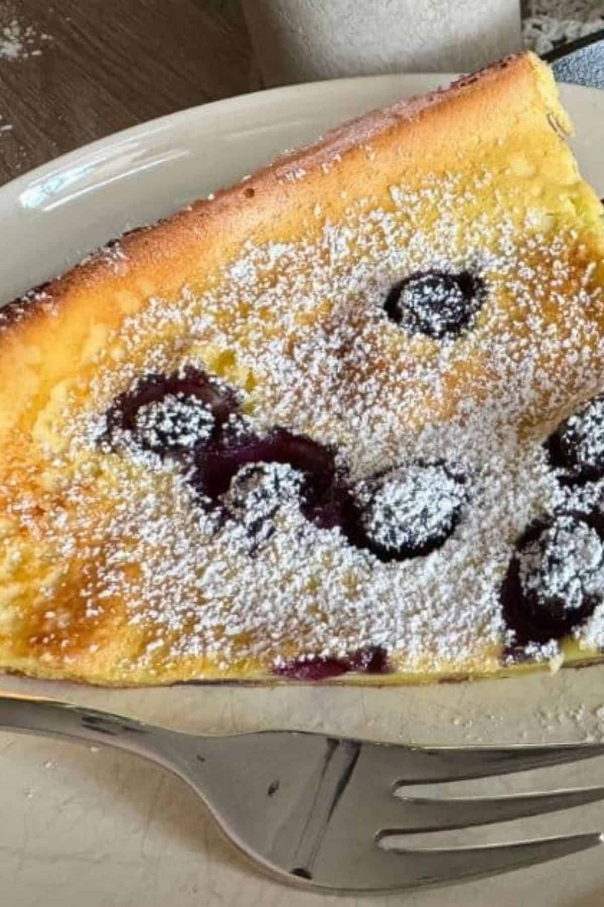 Blueberry Dutch Baby Pancake on a plate, with another pancake blurred in the background.
