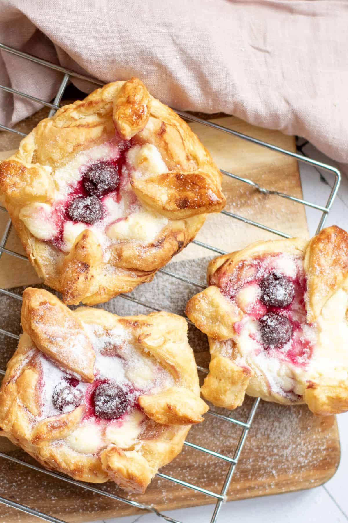 Danish pastries with cream cheese and cherries cooling on a wire rack.