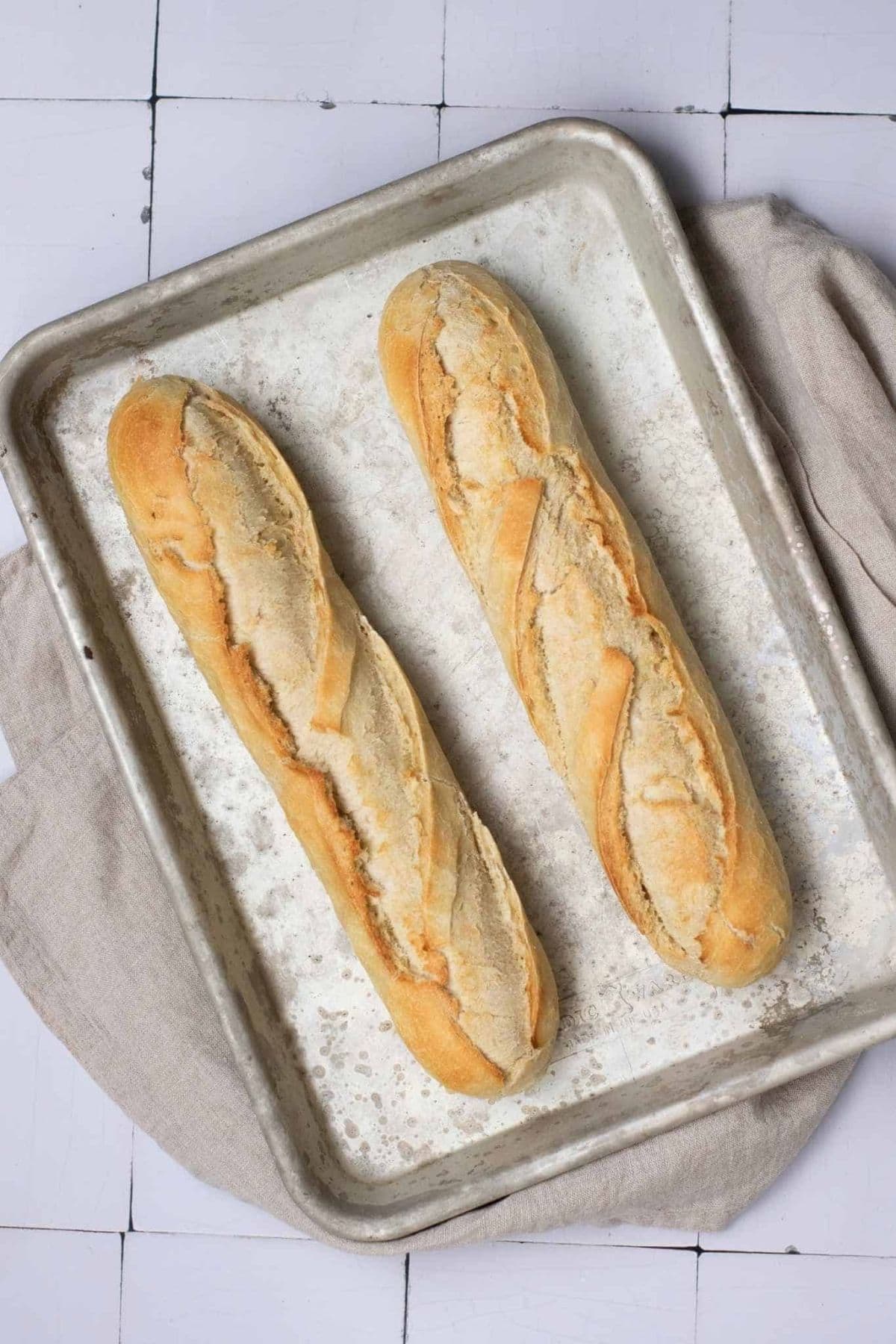French baguette with yeast resting on a baking tray lined with parchment paper.