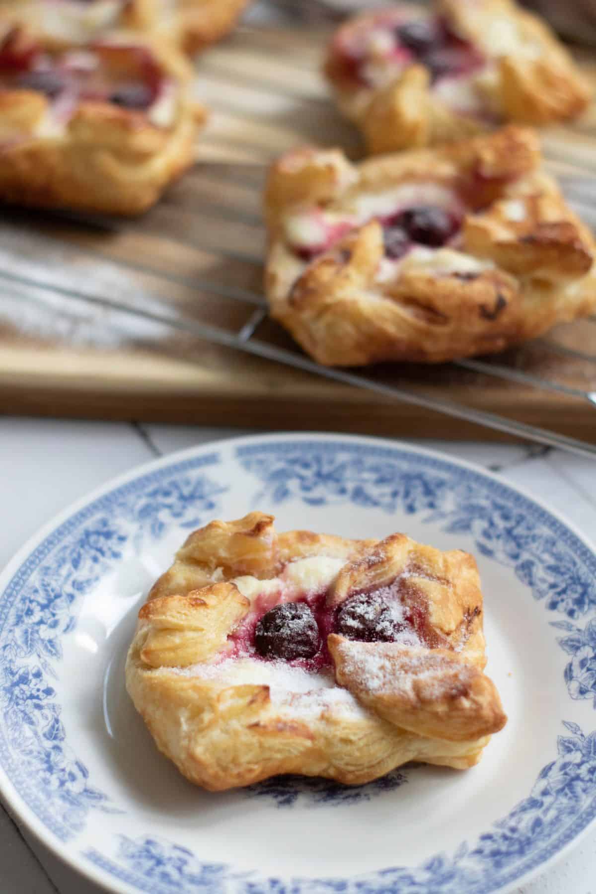 Danish Pastries with cream cheese and cherries, topped with powdered sugar and served on a plate.