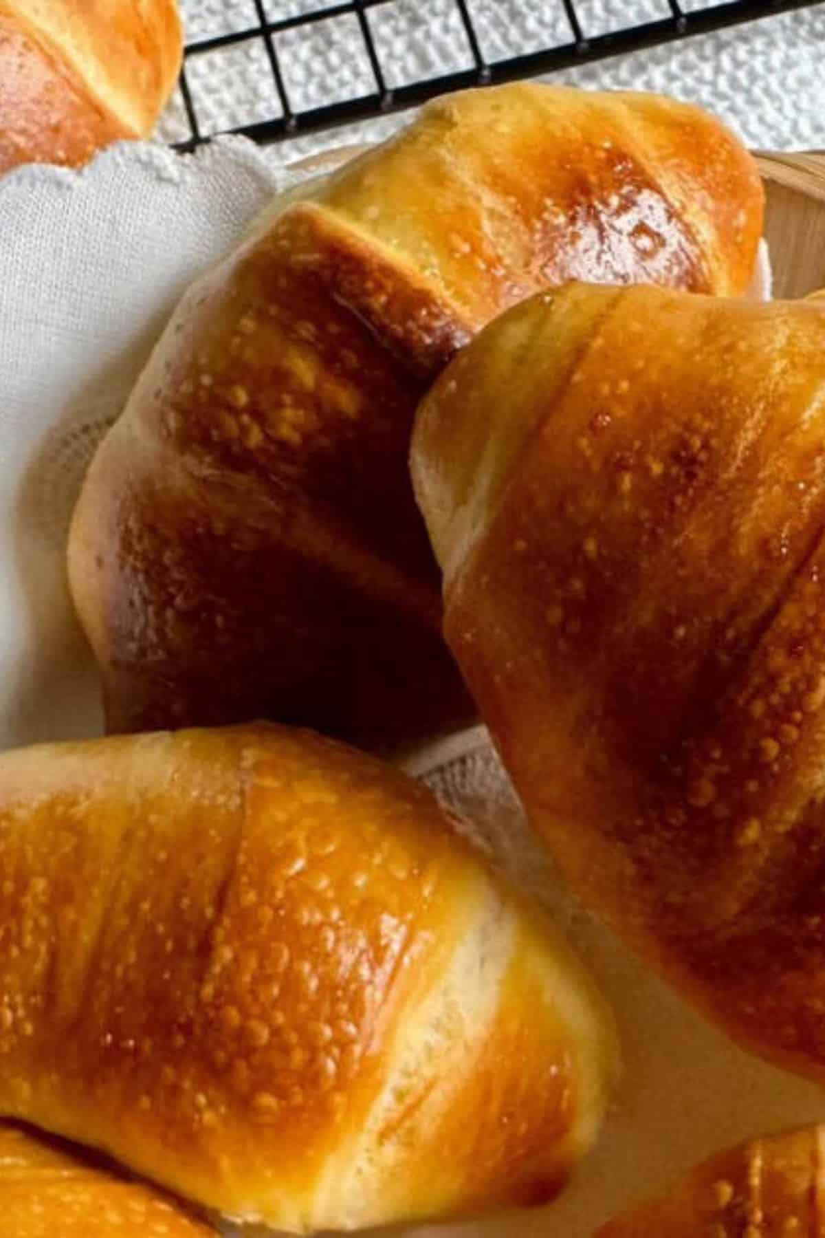 Sourdough crescent rolls in a basket with additional rolls resting on a wire cooling rack.