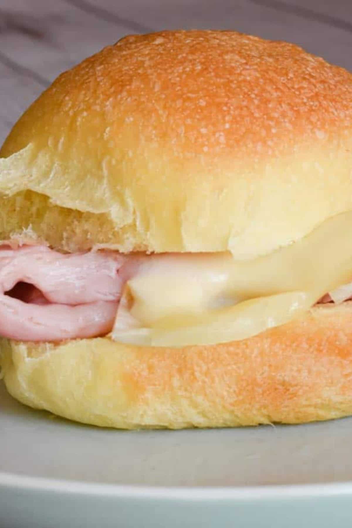 A single sourdough potato roll on a plate, filled with ham and cheese.