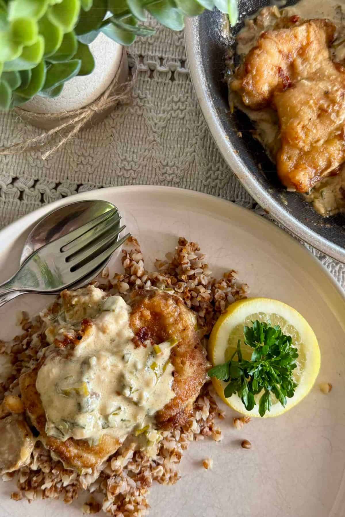 Creamy Lemon Chicken Thighs with Dijon and Parsley served with a lemon slice and buckwheat rice on a plate.