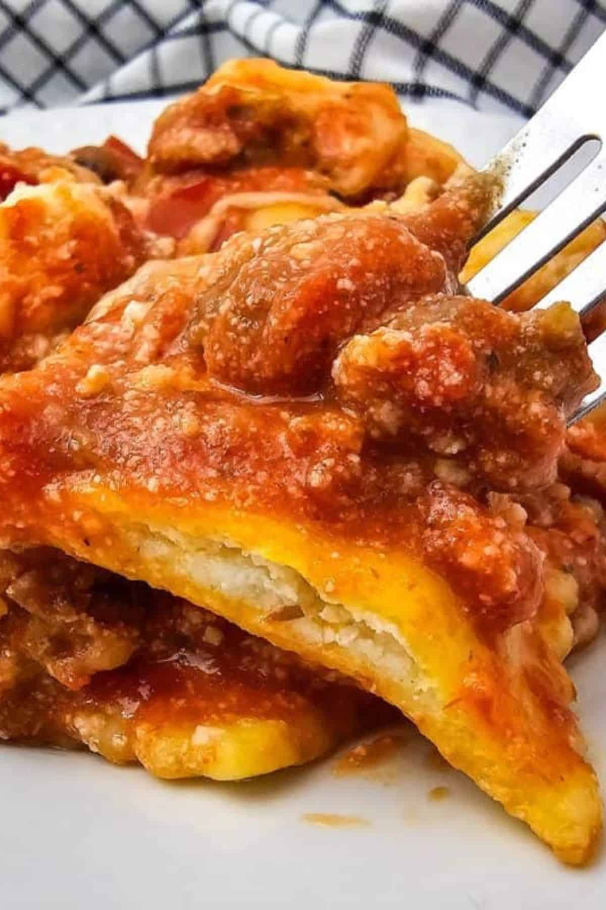 A close-up of cheesy lasagna with a fork lifting a bite.