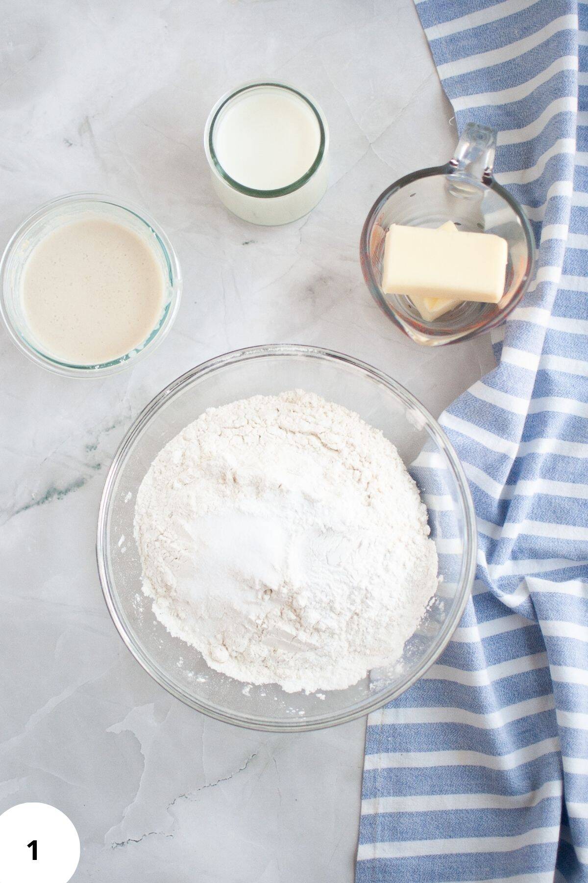 Dry ingredients being mixed in a large bowl with other ingredients placed around it.