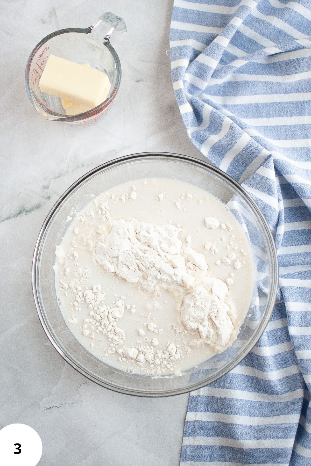Dry and wet ingredients being mixed in a bowl with butter on the side.