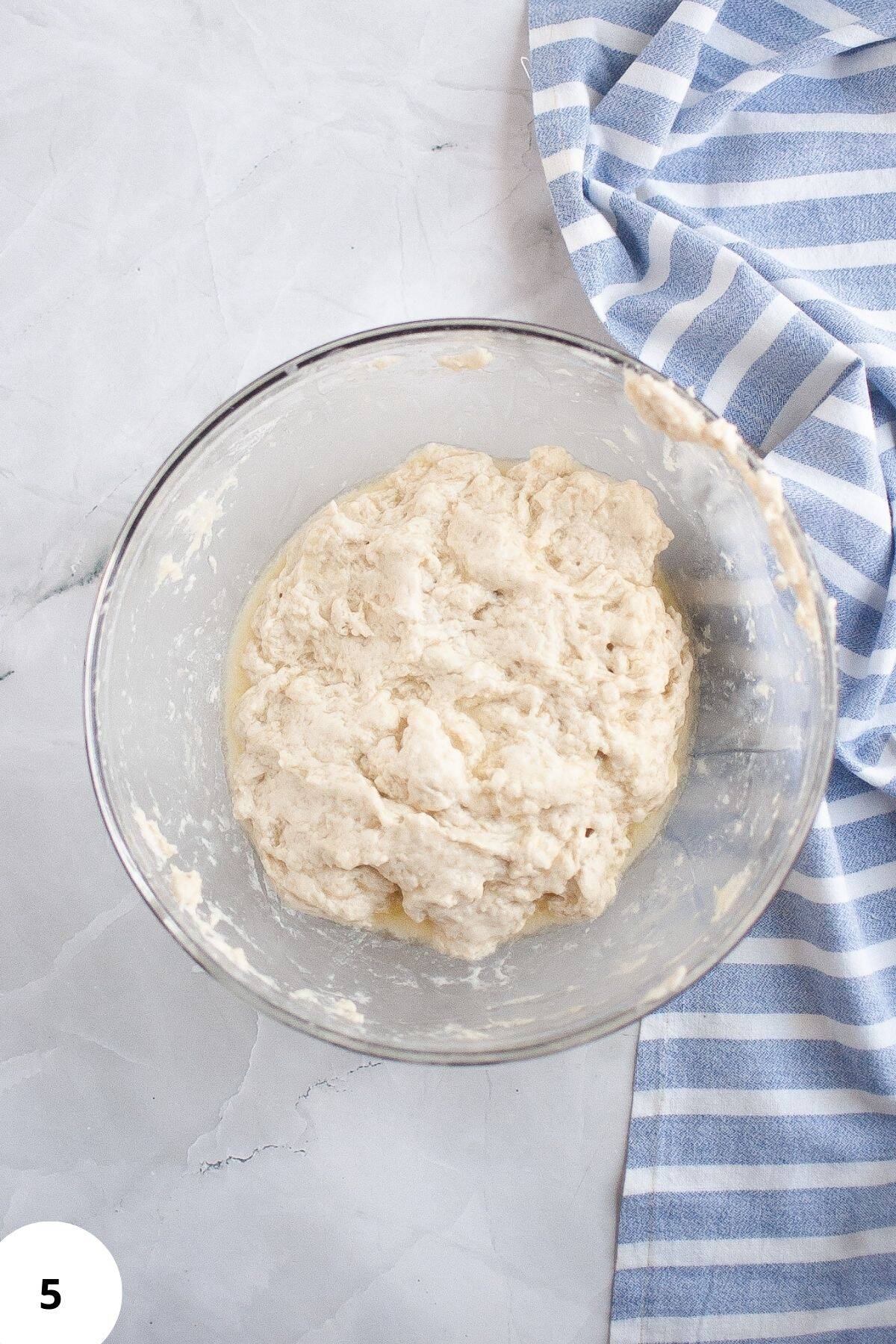 Dough resting in a large mixing bowl with a cloth placed on the side.