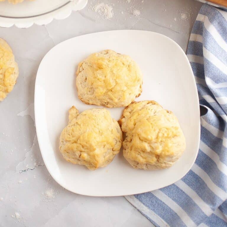 Three muffins served on a plate, with a cloth napkin placed beside them.