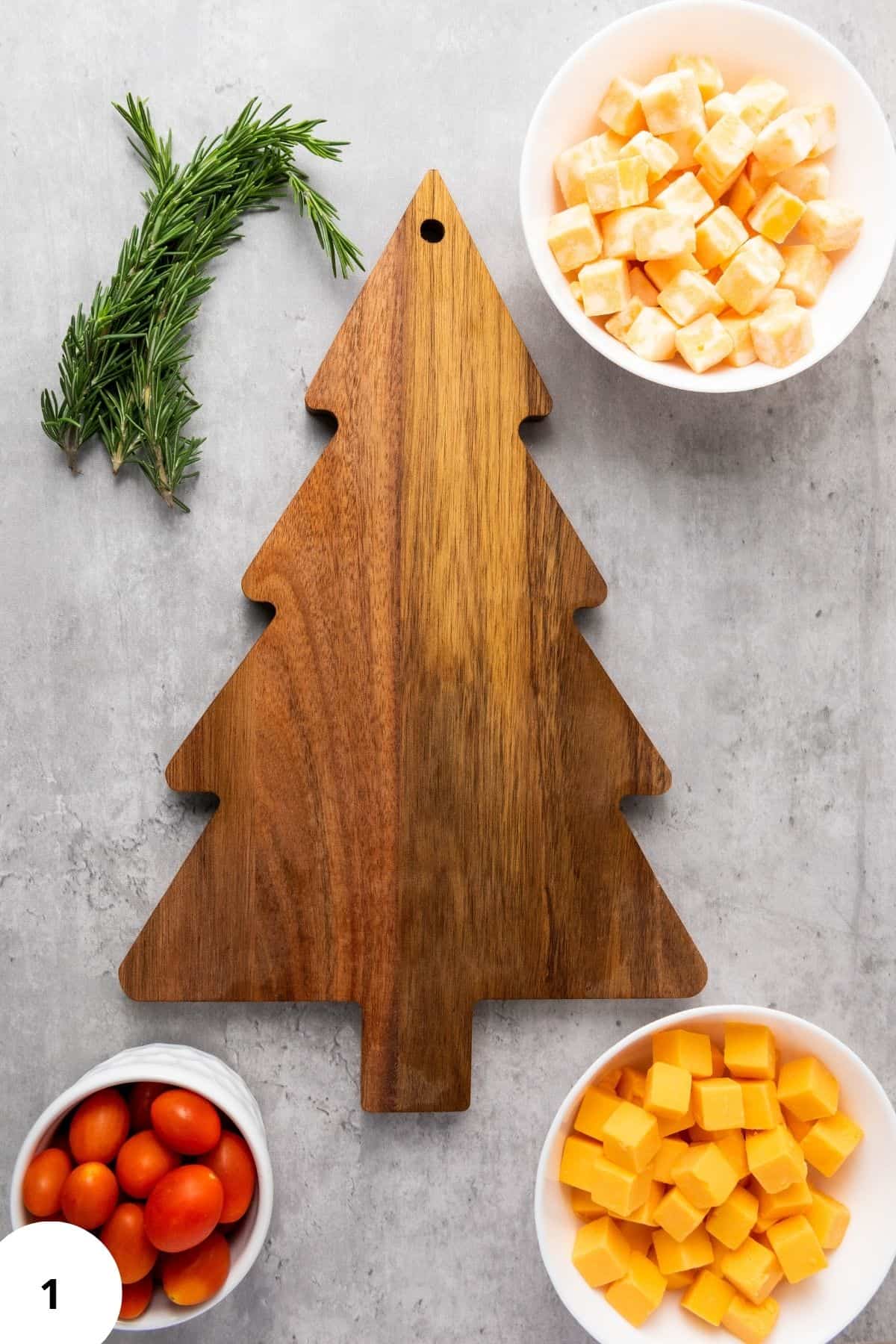 Christmas Tree Cheese Platter on a tree-shaped board surrounded by Colby Jack and Gouda cubes cherry tomatoes and fresh rosemary.