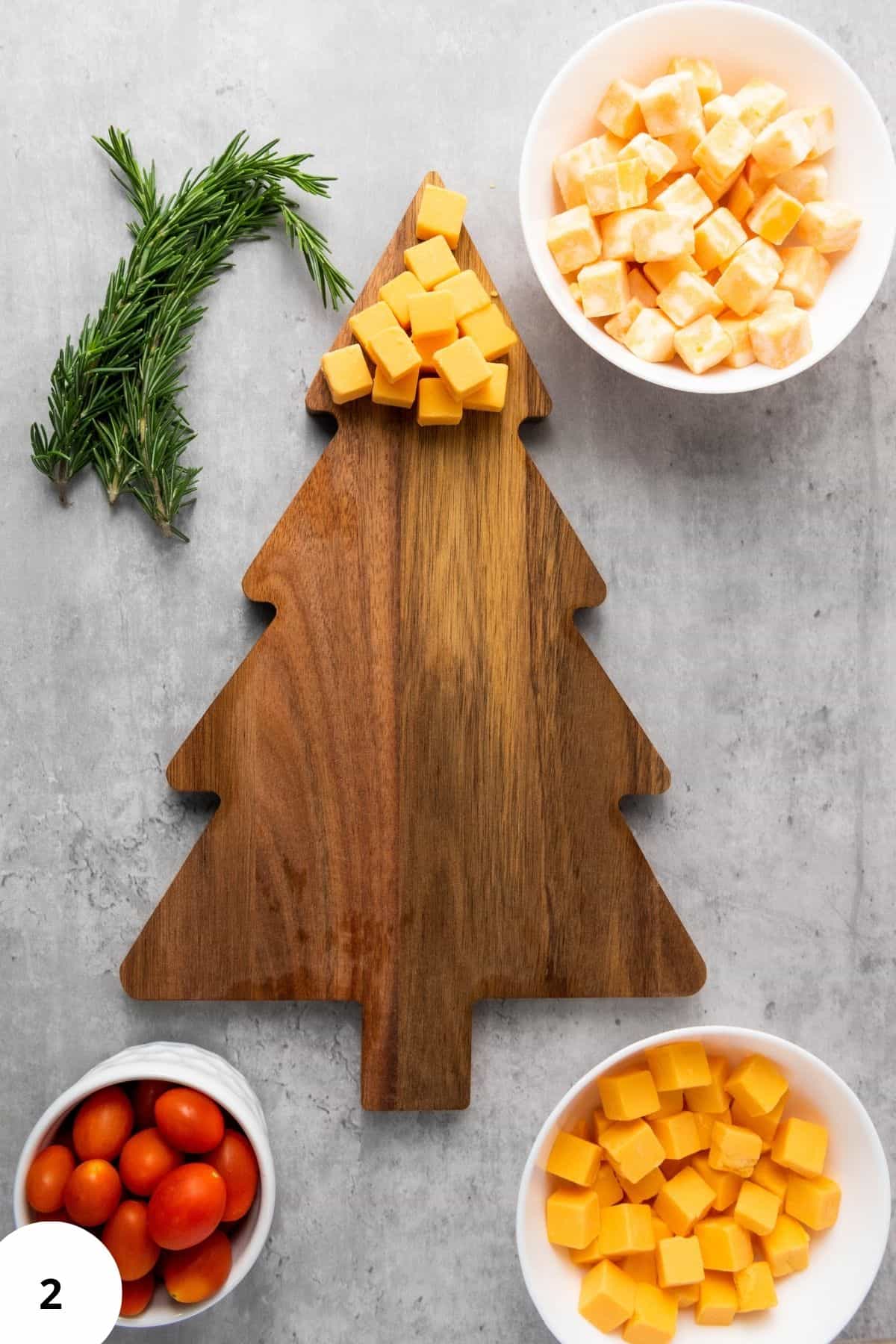 Cheese being arranged on a Christmas tree-shaped board surrounded by figs and other festive ingredients.