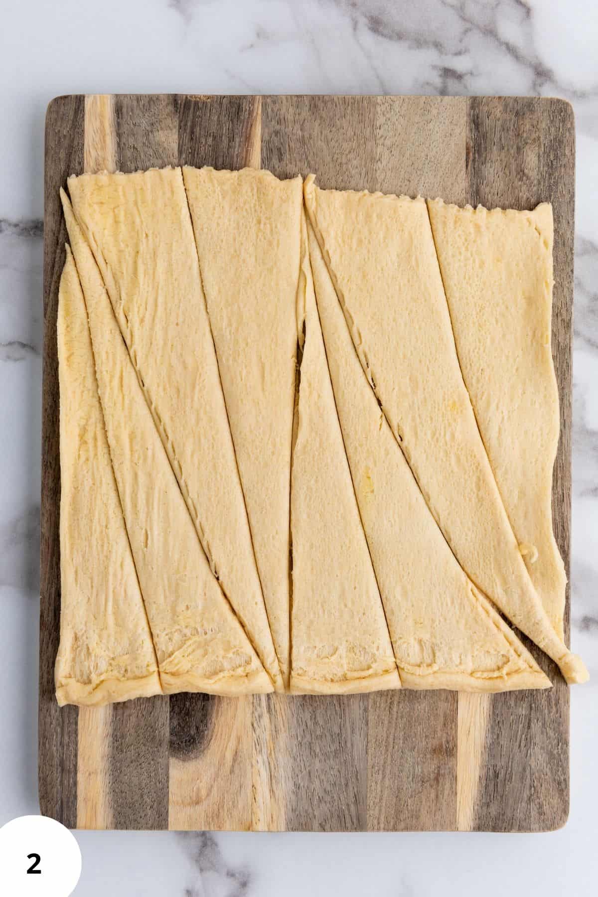 Dough being cut into smaller triangles on a wooden board.