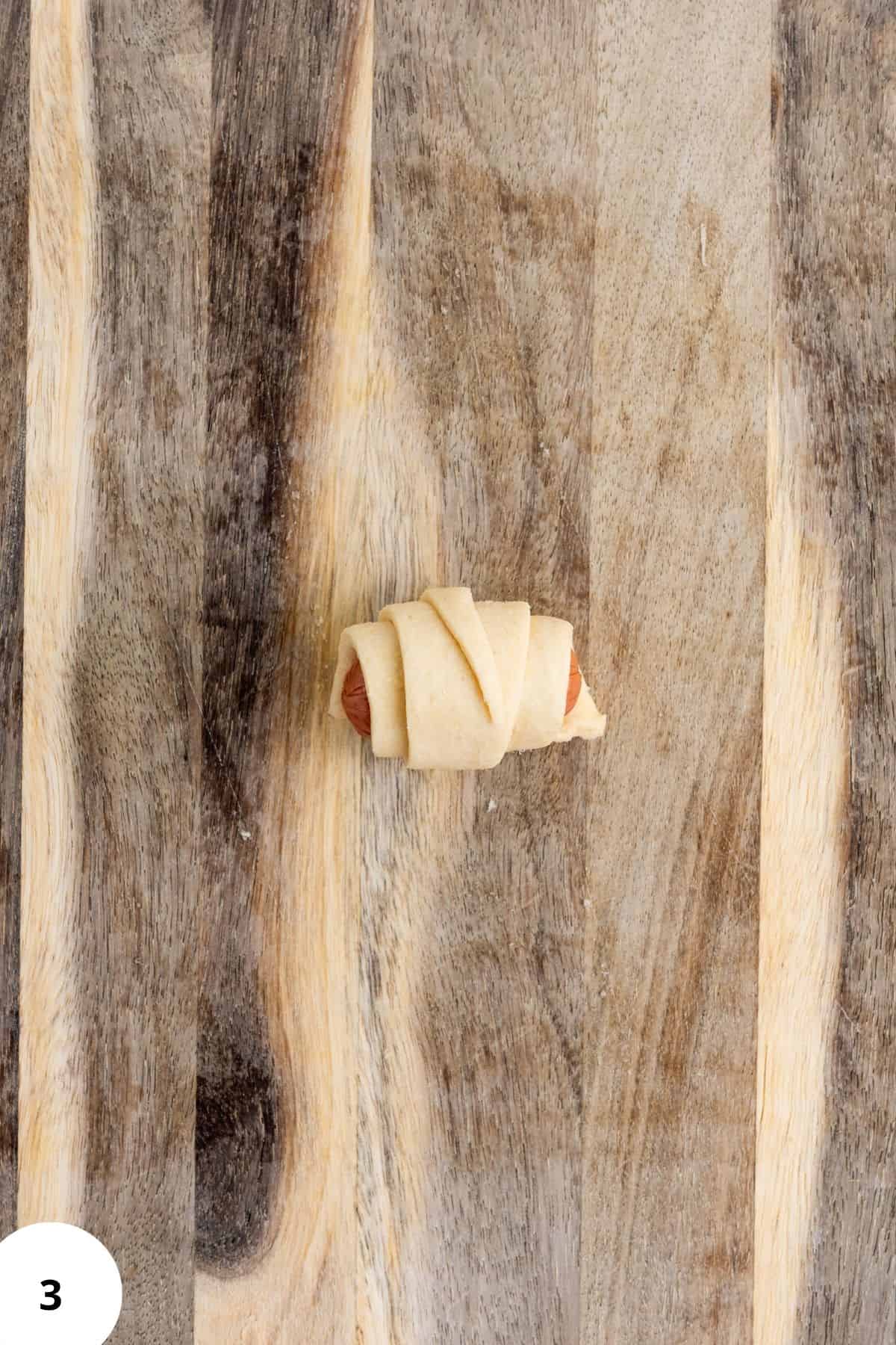 Rolled mini piggies in croissant dough on a wooden board.
