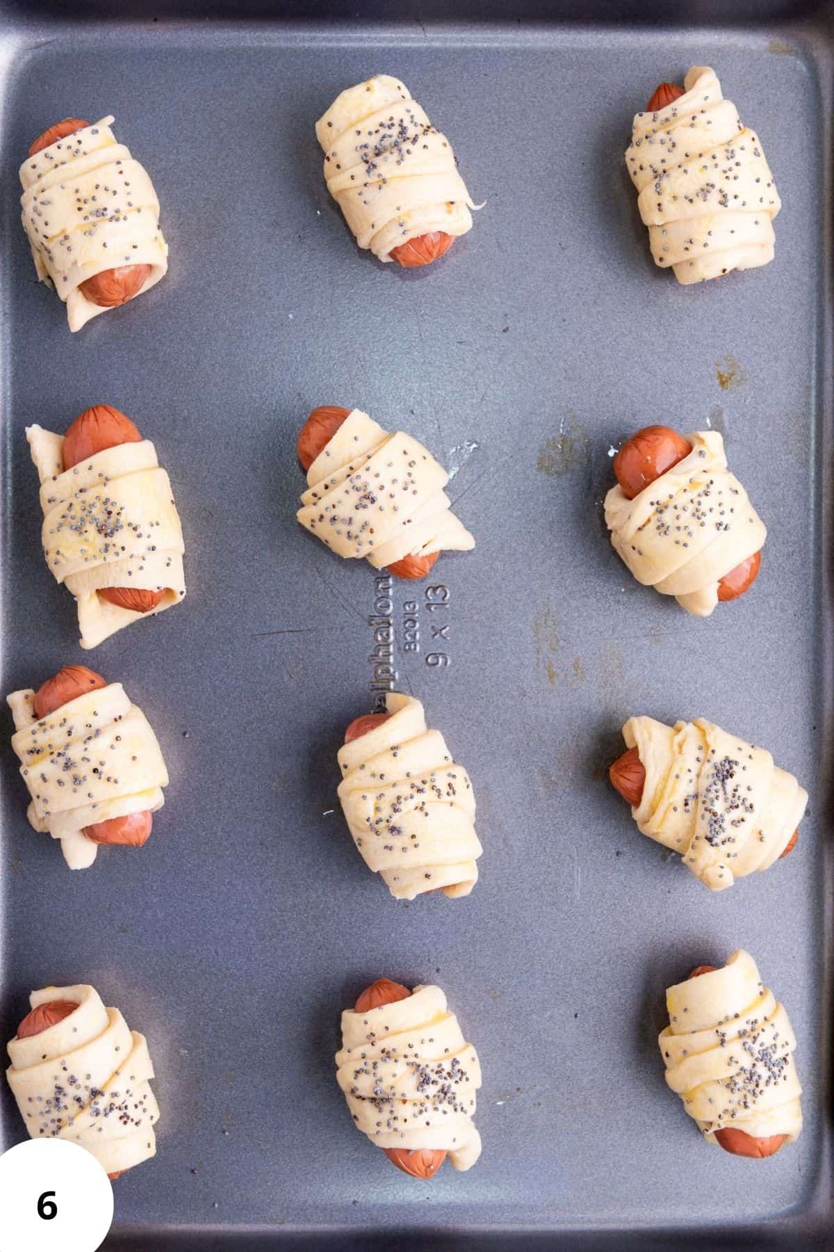 Unbaked mini piggies in croissant dough arranged on a parchment-lined baking tray.