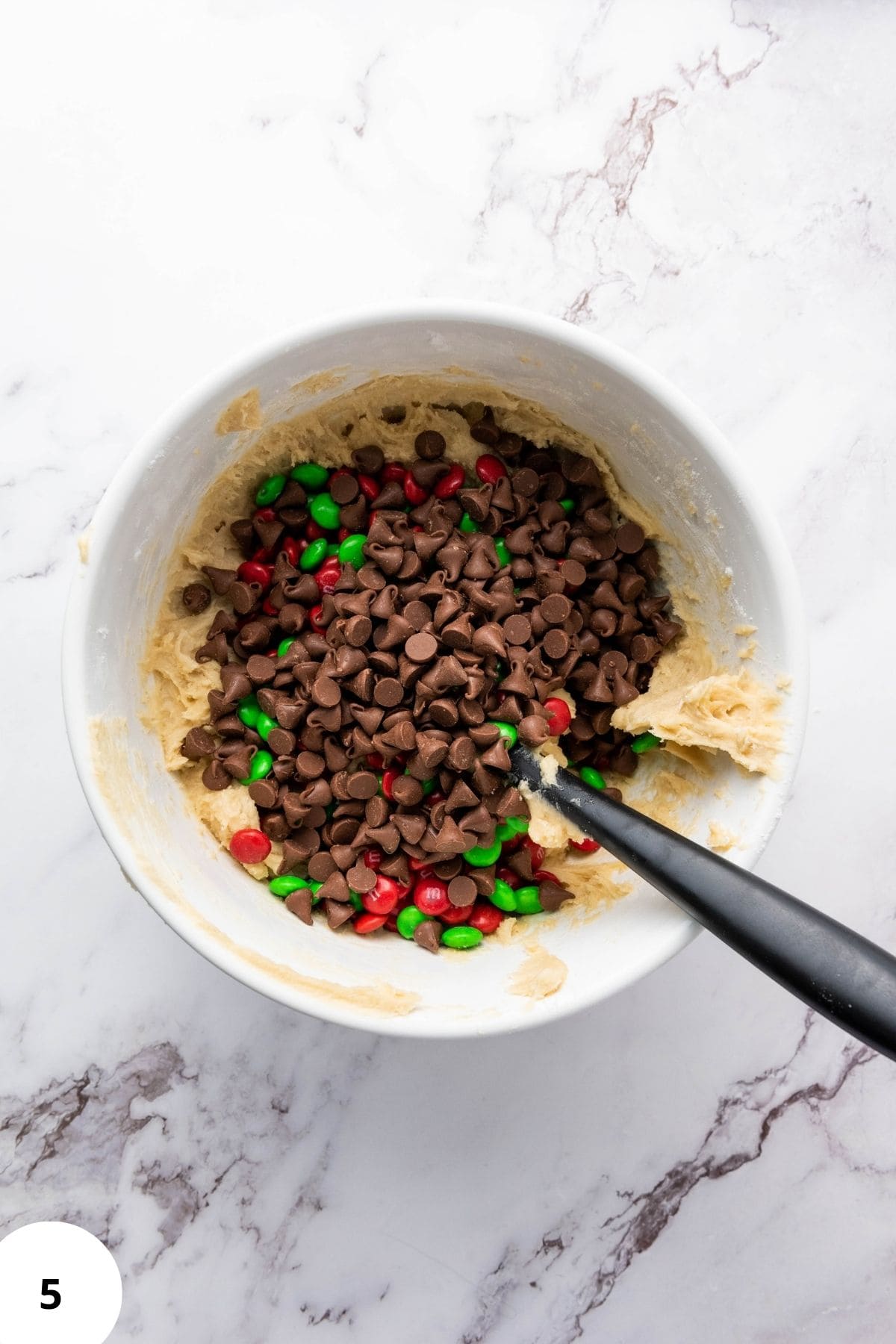 Cookie ingredients being mixed in a bowl with a spatula resting on the side.