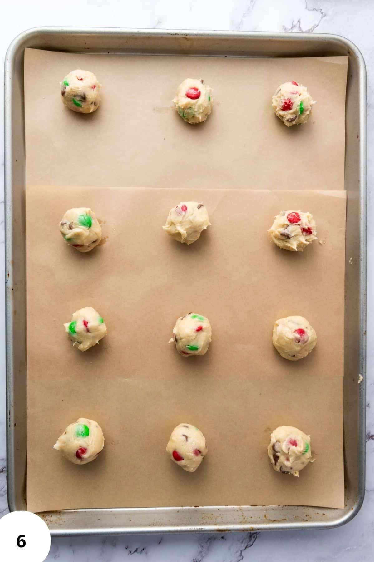 Scooped cookie dough lined on parchment paper in a baking pan, ready to bake.