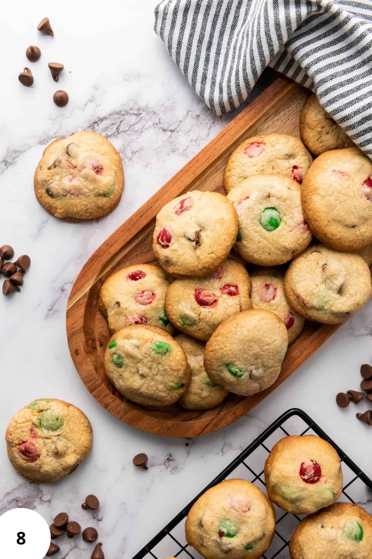 A stack of Christmas M&M cookies served on a wooden board with colorful candies visible with cloth underneath.