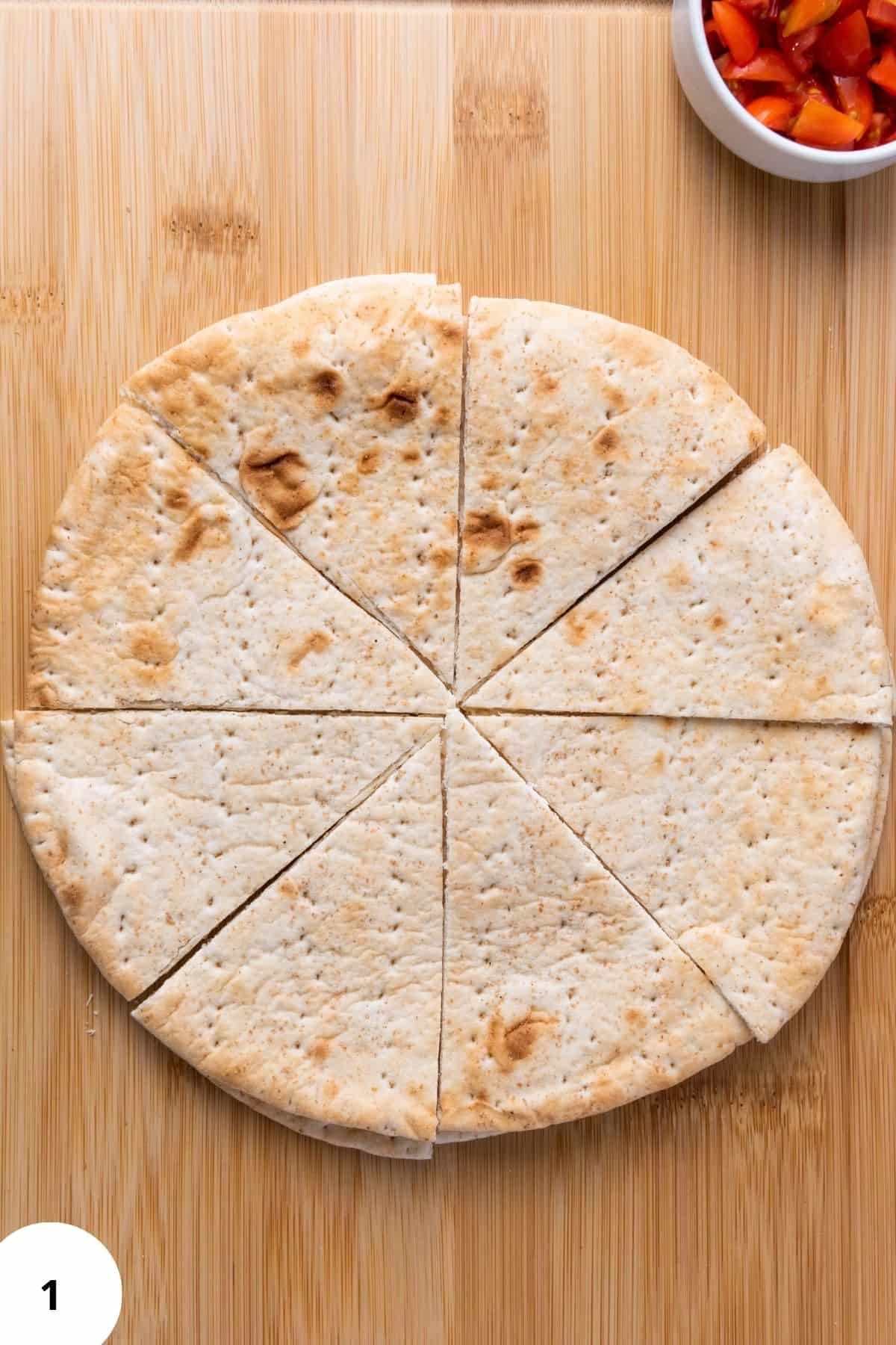 A pita bread sliced into triangular wedges on a cutting board, ready for topping.
