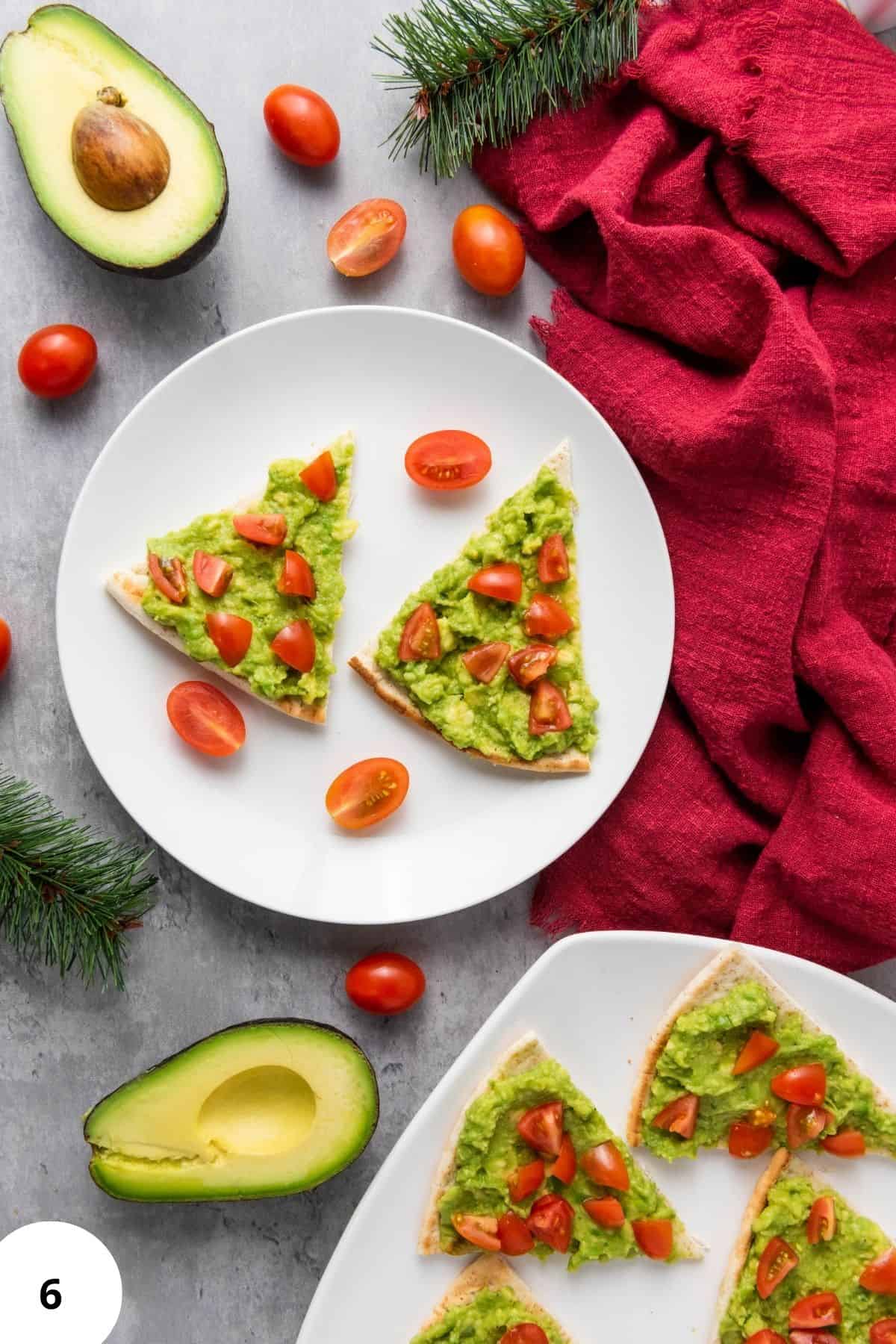 Avocado pita tree on a plate with cherry tomatoes and avocado, set with festive holiday decorations in the background.