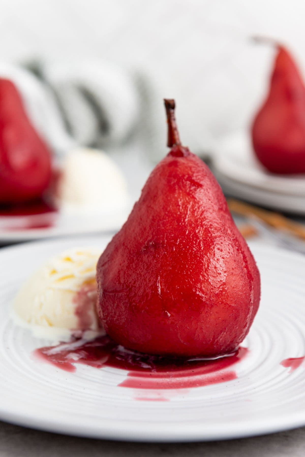 A plate with a single red wine poached pear in the center served with a scoop of vanilla ice cream.