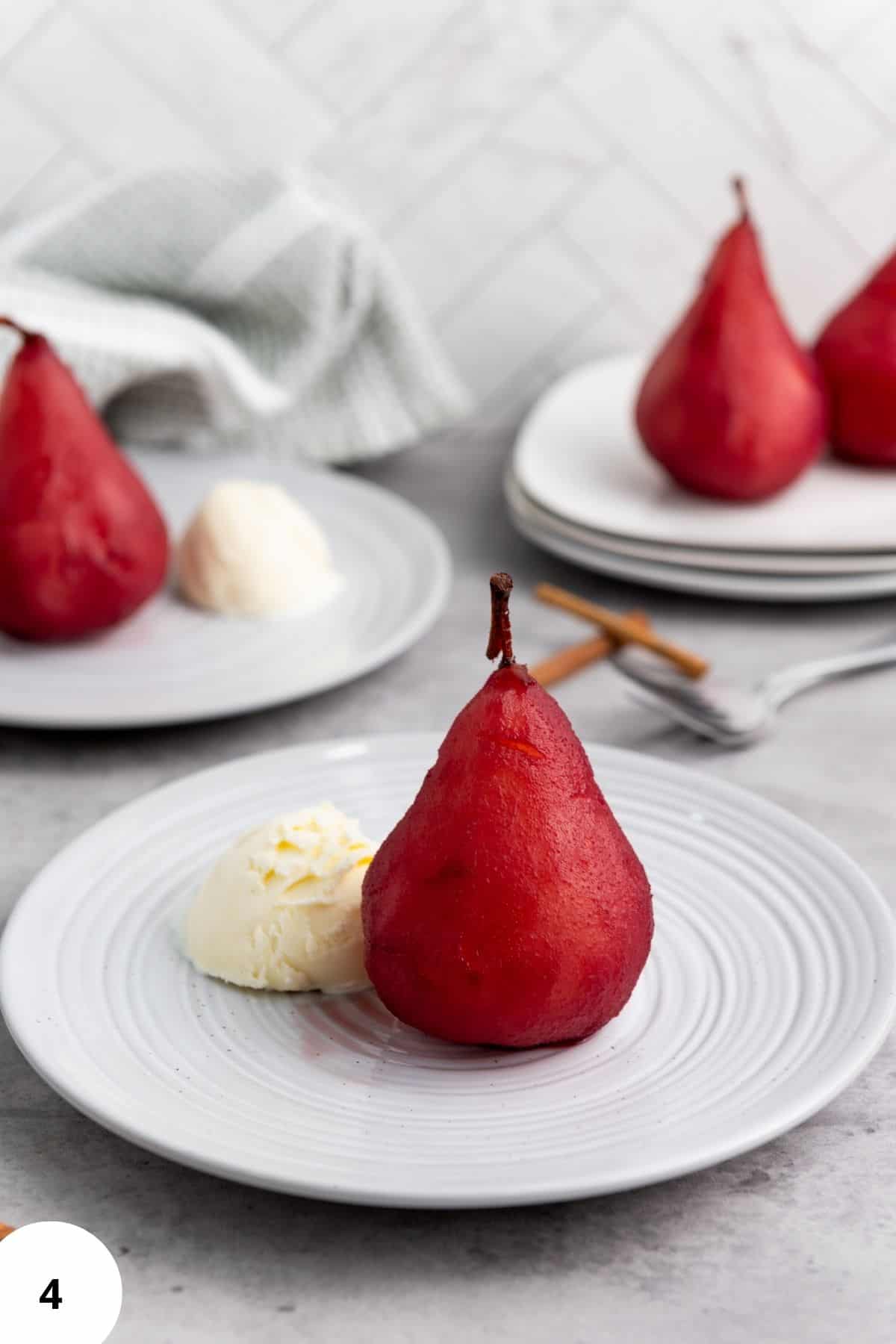 A plates with a red wine poached pear in the center served with a scoop of vanilla ice cream.