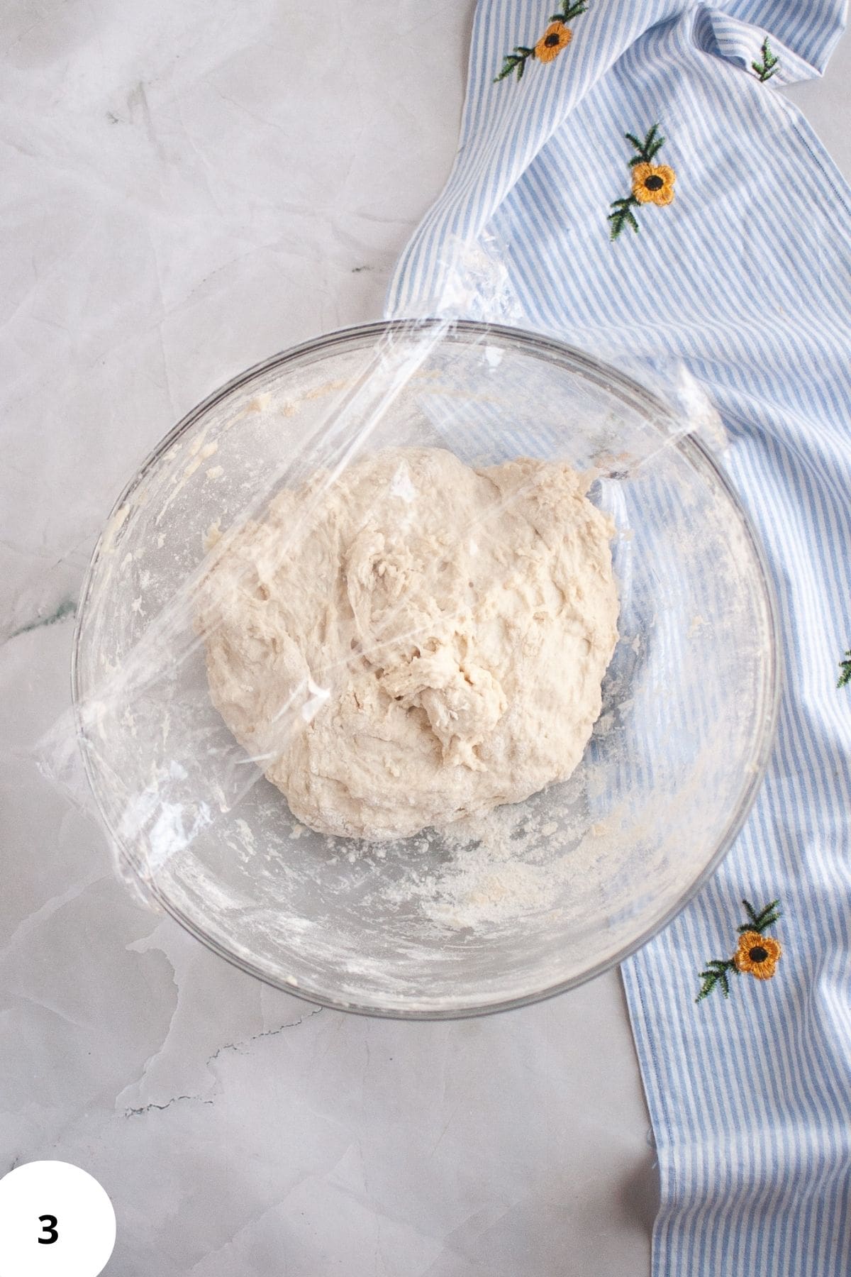 Sourdough dough resting in a bowl covered with plastic wrap.