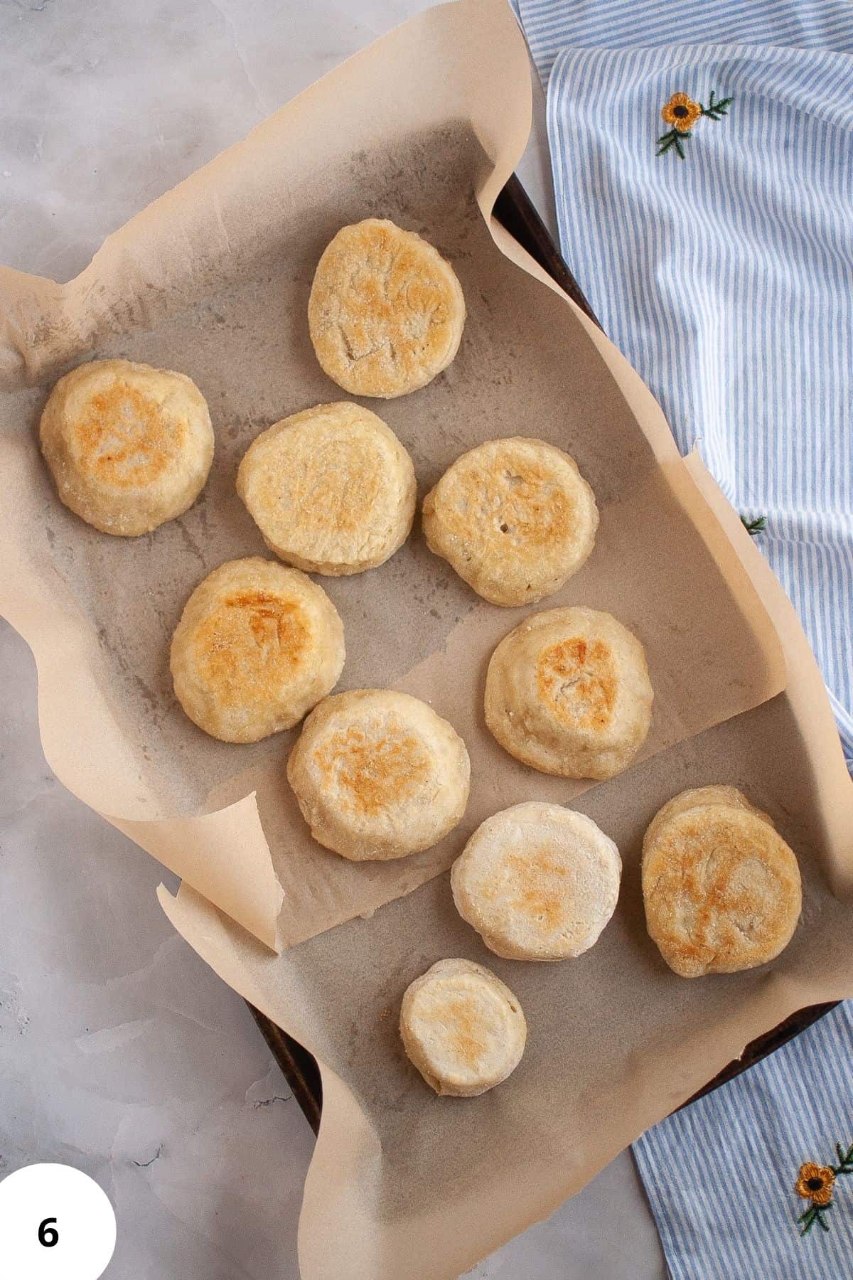 Freshly baked sourdough English muffins resting in a skillet lined with parchment paper.