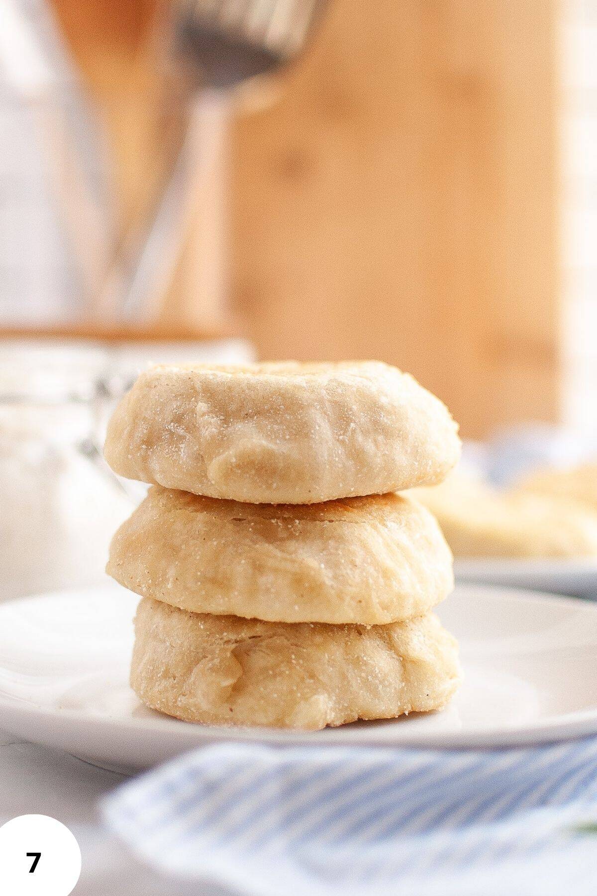 Stack of golden sourdough English muffins served on a plate with a cloth napkin underneath.
