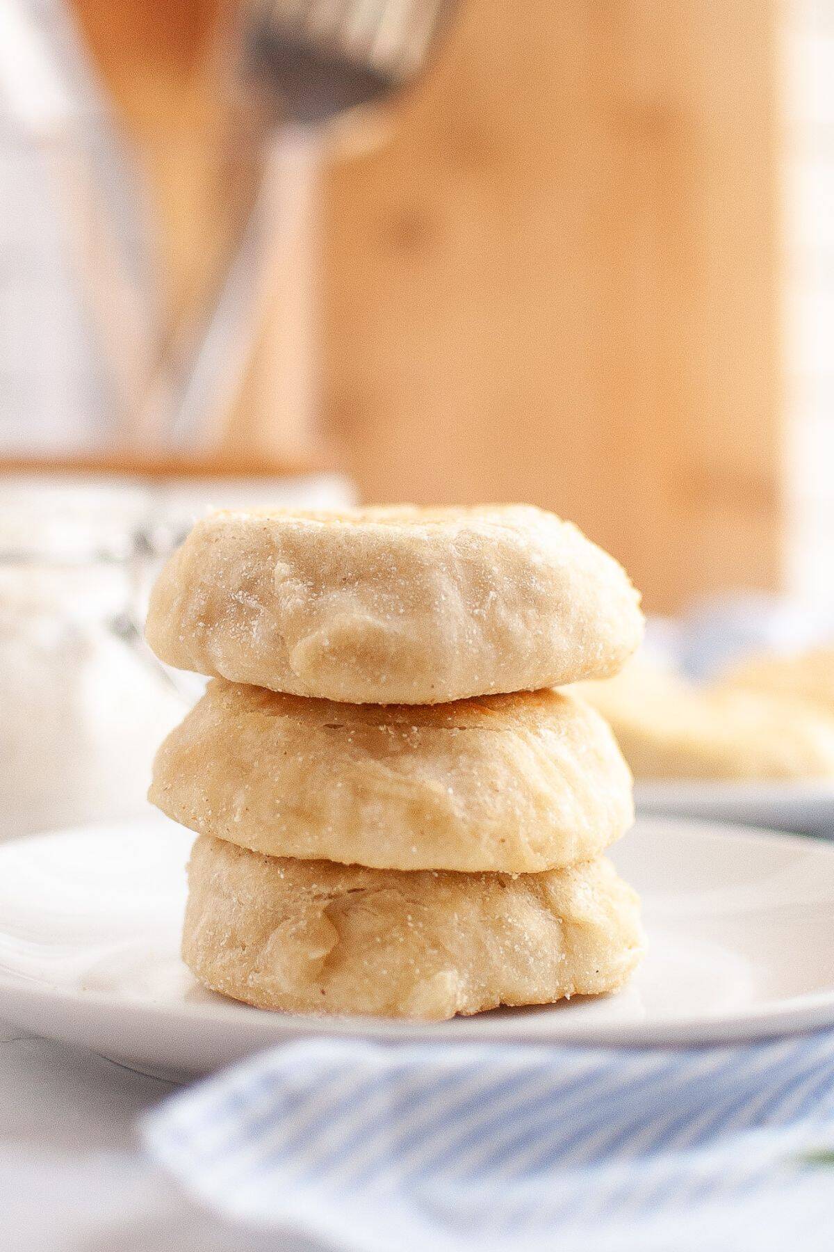 Stack of golden sourdough English muffins served on a plate with a cloth napkin underneath.