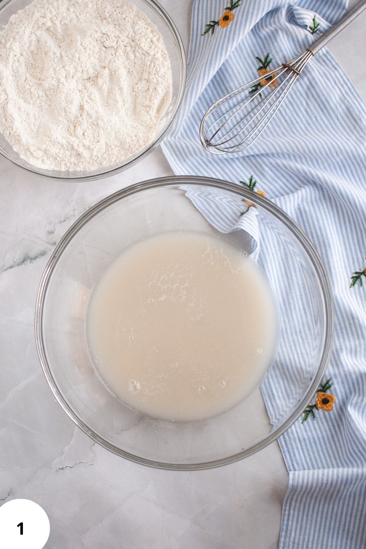 Ingredients such as water and starter being mixed in a large bowl with flour in a separate bowl on the side.
