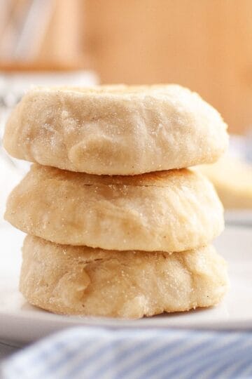 Stack of golden sourdough English muffins served on a plate with a cloth napkin underneath.
