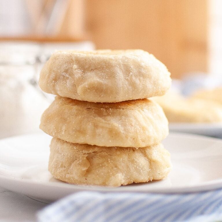 Stack of golden sourdough English muffins served on a plate with a cloth napkin underneath.