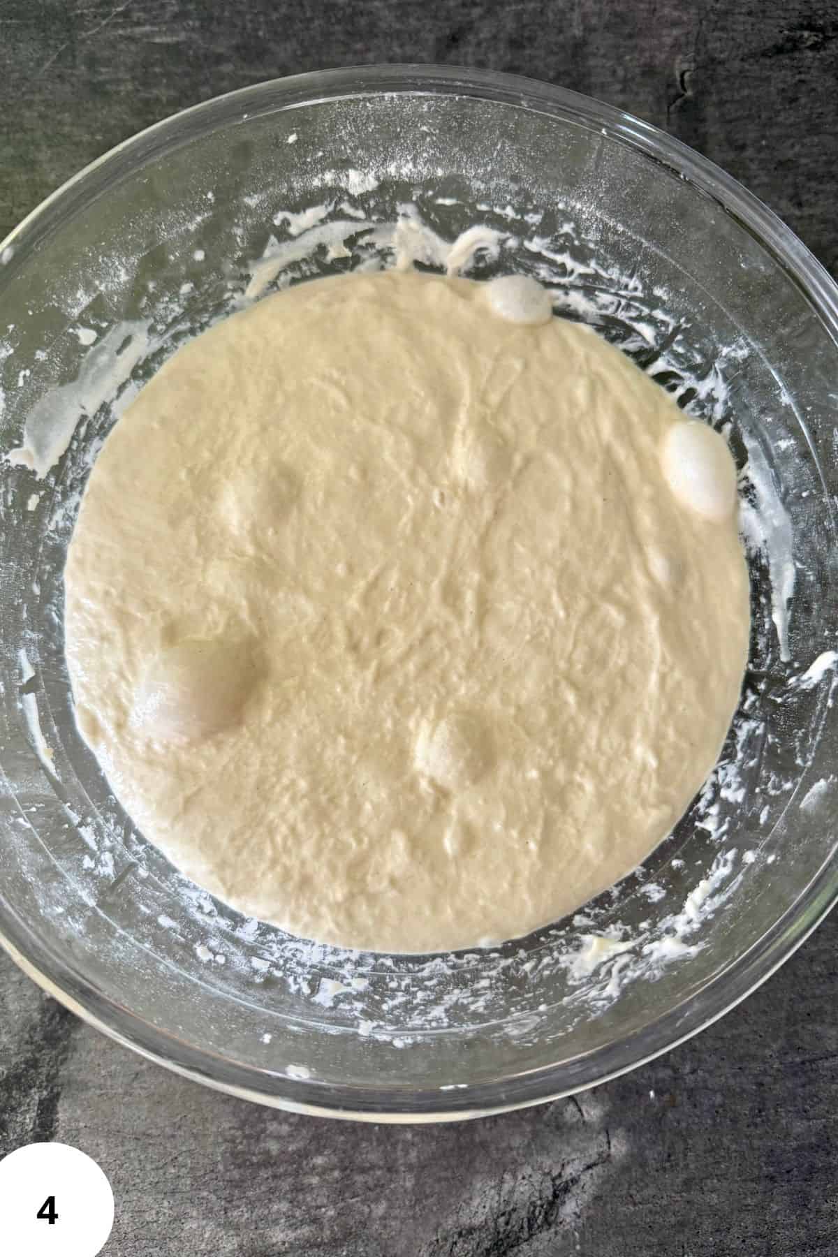 Dough resting in a mixing bowl with visible bubbles forming on the surface.