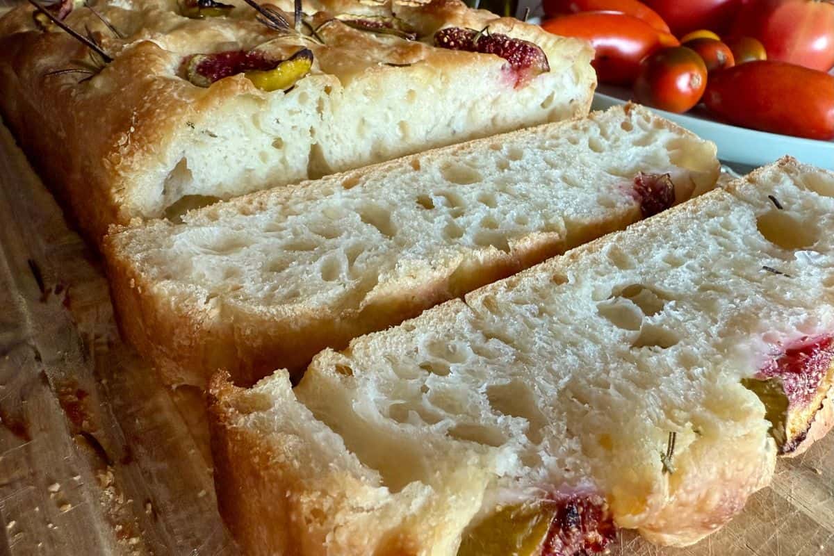 Close-up of freshly baked sourdough focaccia being sliced on a wooden cutting board, showing its soft, airy interior and golden crust.