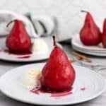 A plate with a single red wine poached pear in the center served with a scoop of vanilla ice cream.