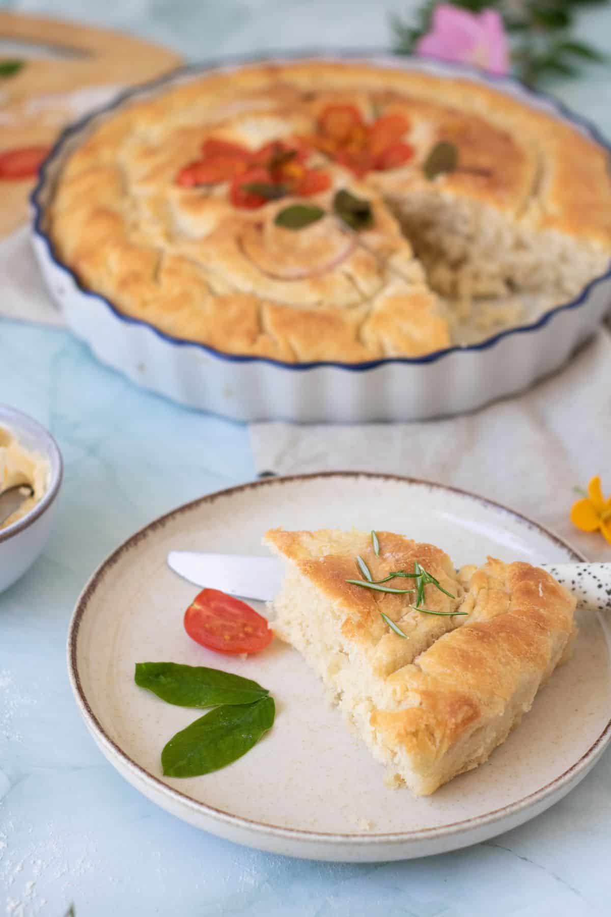 Homemade focaccia topped with cherry tomatoes and onion, sliced on a plate and surrounded by fresh cherry tomatoes.