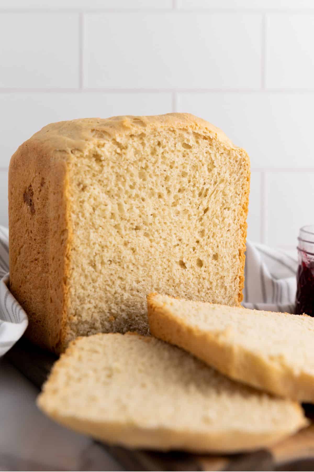 Bread machine white bread loaf with slices cut, served with a side of jam.