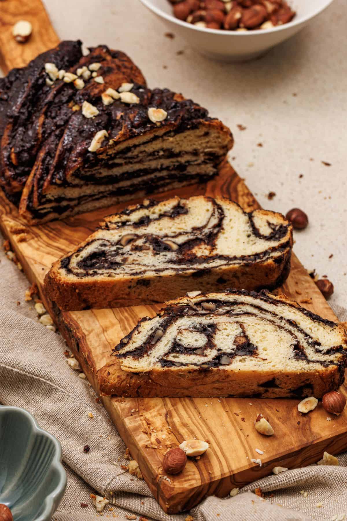 Chocolate babka loaf with several slices arranged on a wooden board, showing the swirled chocolate filling inside.