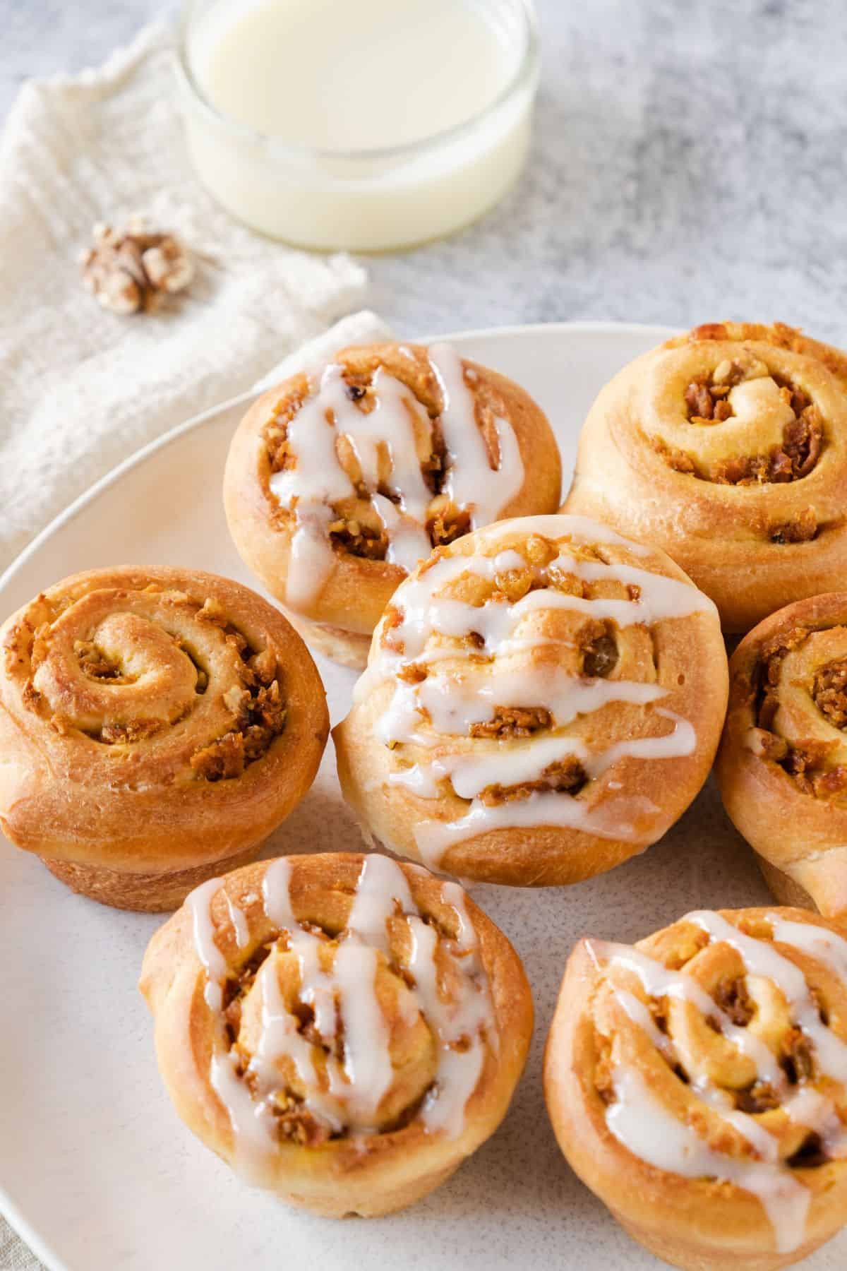 Carrot cake cruffins drizzled with cream cheese frosting, served on a plate.