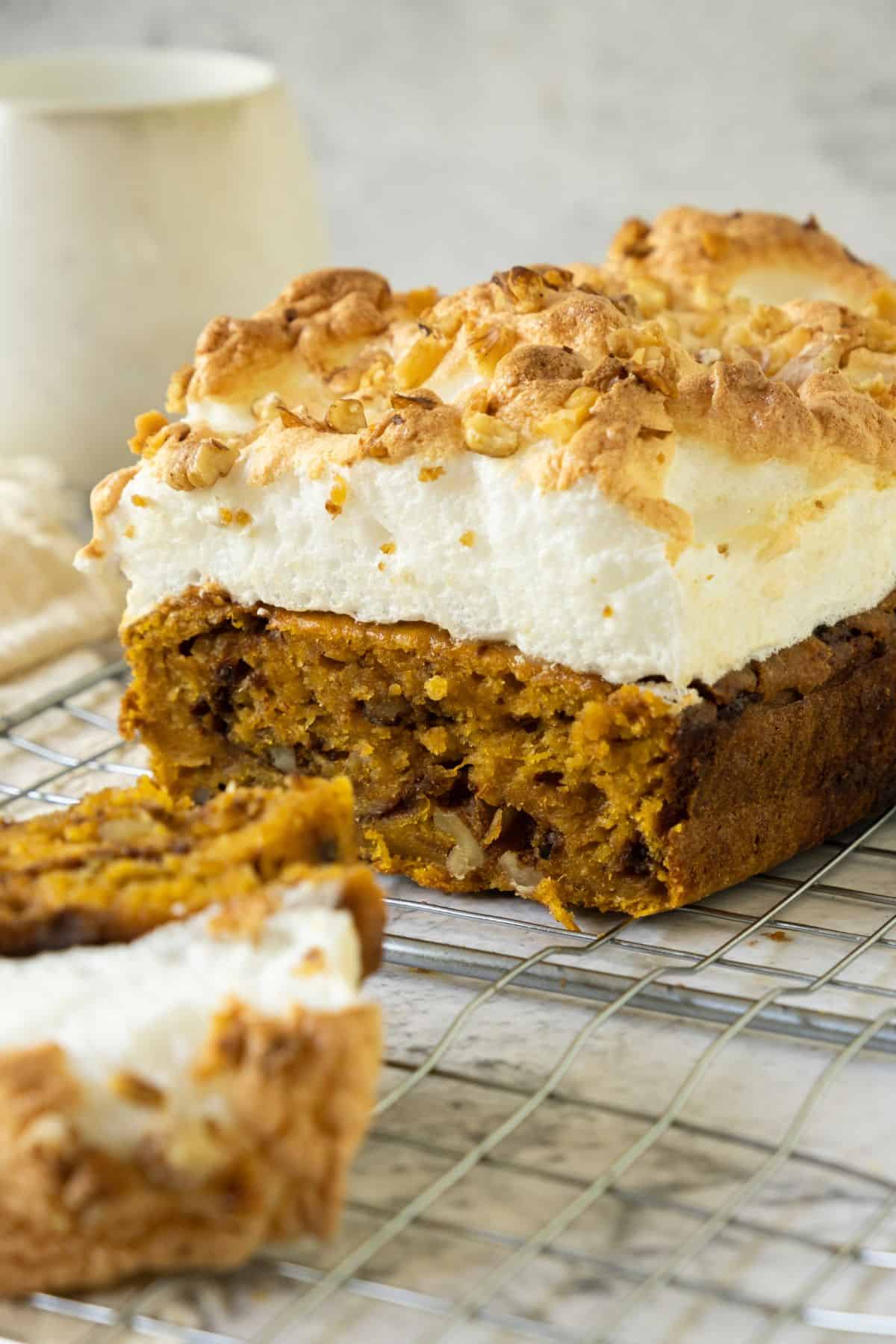 Close-up of sweet potato quick bread topped with golden fluffy meringue, with a slice placed on a wire cooling rack.