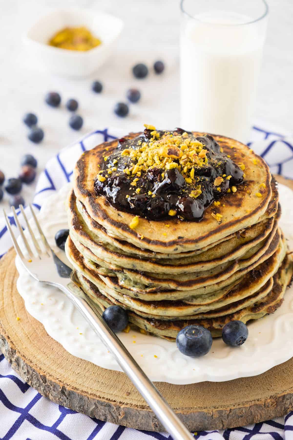 Stacked fluffy pancakes topped with blueberry jam, surrounded by fresh blueberries.