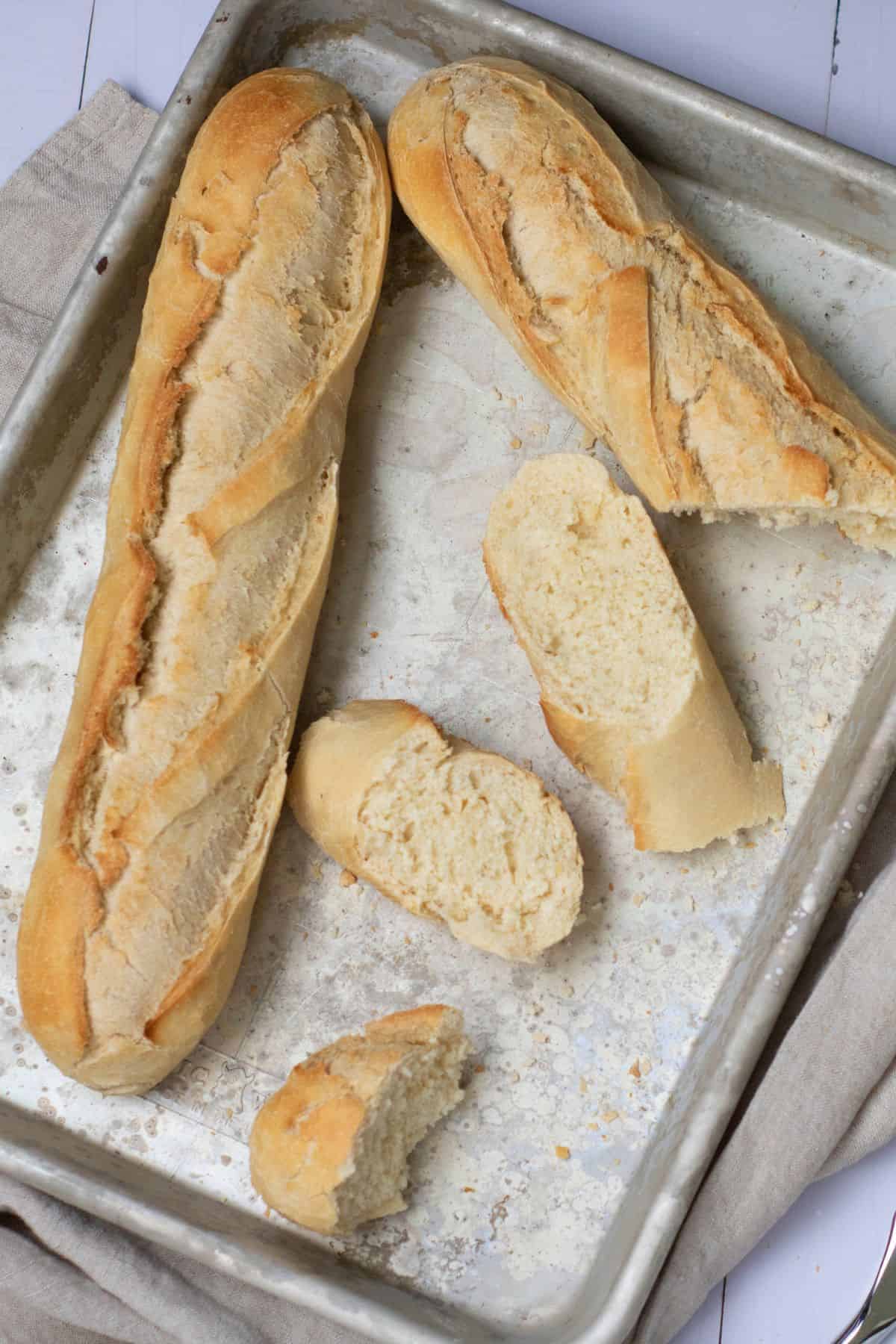 Homemade French baguette in a baking pan with several slices cut, showing the soft interior and golden crust/