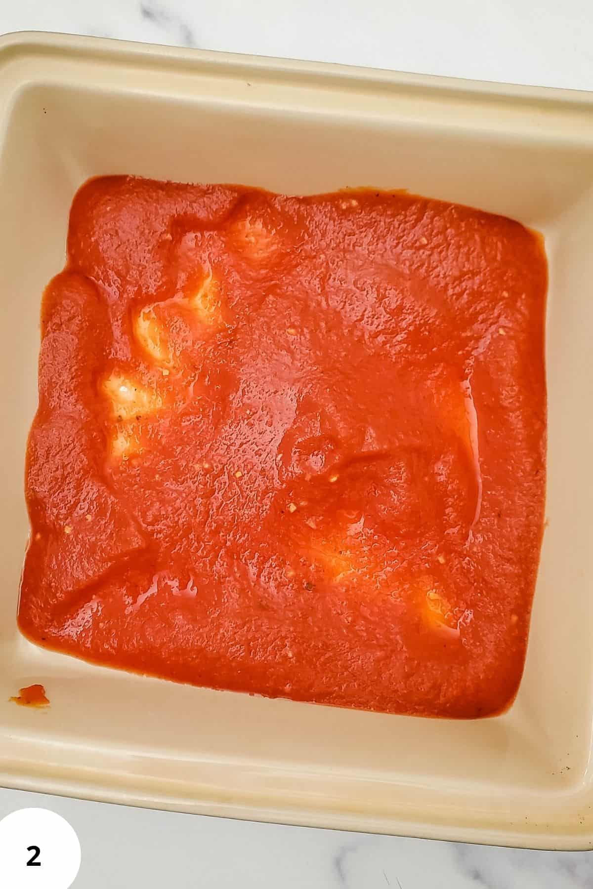 Pasta sauce spread on the bottom of a casserole dish.